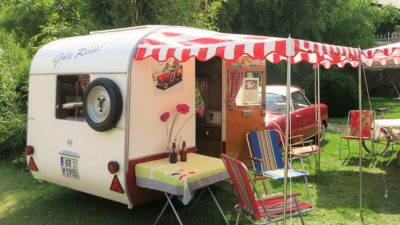 En husvagn med uppslaget regnskydd. Under skyddet är ett bord med en vas på och ett par stolar.