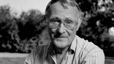 En svartvit bild av Ingvar. Han har stora glasögon och ganska många rynkor. Hans hår är kort och blont, och han har en randig skjorta på sig.