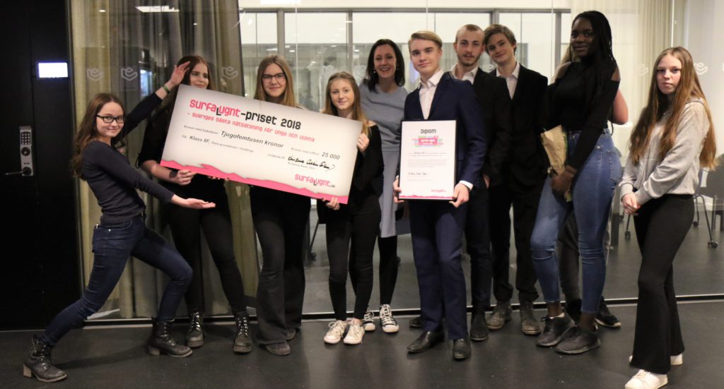 Delar av klass 8F står uppradade framför kameran. Några av eleverna håller i en stor check på 25000 kronor. En annan elev håller i ett diplom.