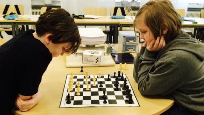 Två barn sitter mitt emot varandra i ett klassrum och tittar på ett schackbräde som ligger på bordet.