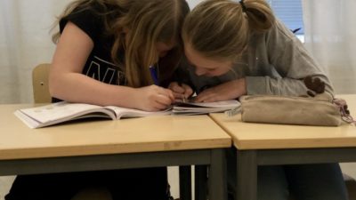 Två barn sitter bredvid varandra och skriver i en skolbok tillsammans.