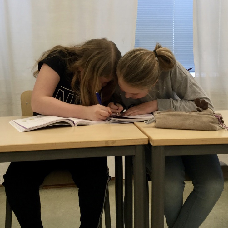 Två barn sitter bredvid varandra och skriver i en skolbok tillsammans.