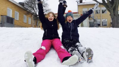 Två barn sitter i en snöig backe på en skolgård.