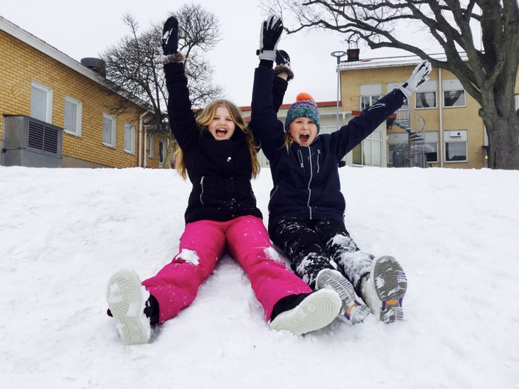 Två barn sitter i en snöig backe på en skolgård.