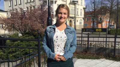 En vuxen med jeansjacka står utomhus och ler in i kameran.