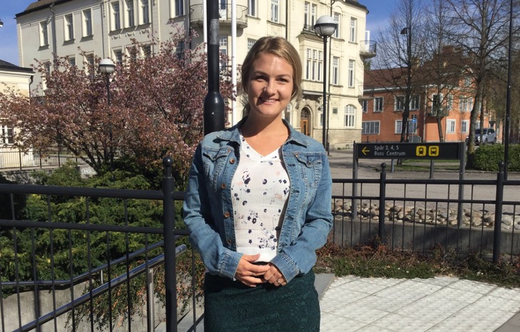 En vuxen med jeansjacka står utomhus och ler in i kameran.