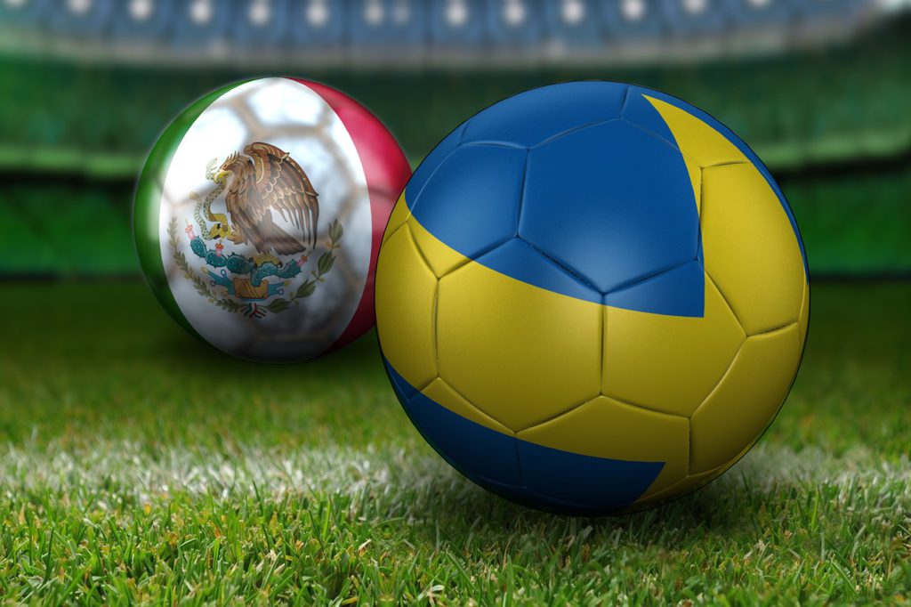 Två fotbollar ligger på en fotbollsplan. Den närmste bollen är helt blå med ett gult kors hela vägen runt. Den andra bollen är grön, vit och rödrandig. På det vita fältet syns en stor örn som sotter på en kaktus.