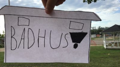 En ritad bild framför ett landskap. På bilden står det "badhus".