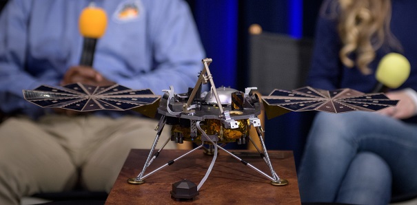 På ett bord står en liten modell av en maskin. Den har tre ben och en metallkropp. På sidorna går det ut två saker som ser lite ut som vingar.