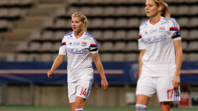 Ada går över en fotbollsplan. Hon har fotbollskläder på sig och sitt hår uppsatt i en tofs. I bakgrunden syns fotbollsläktare.