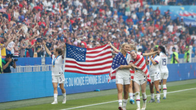 USA:s lag springer längs med kanten av planen. De håller upp en stor amerikansk flagga, vinkar åt publiken och kramar varandra.